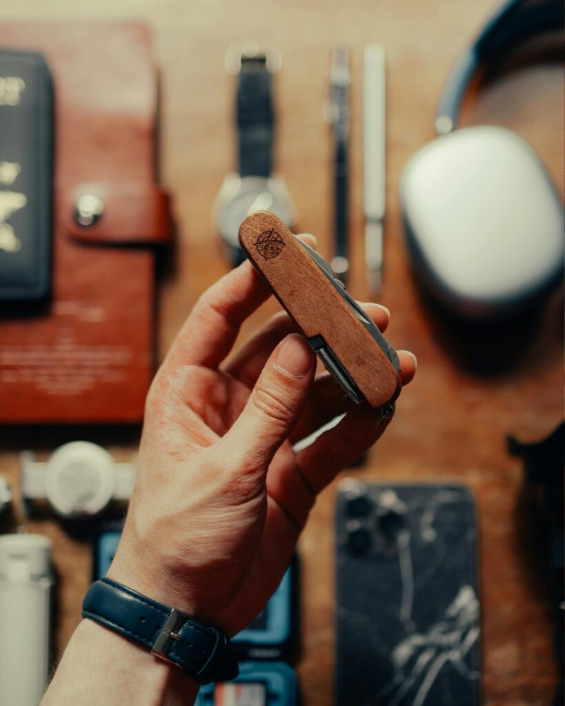 A hand holds a classic wooden pocket knife with accessories on a wooden table.